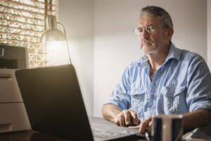 Senior man on computer reading a credit union newsletter about elder financial exploitation